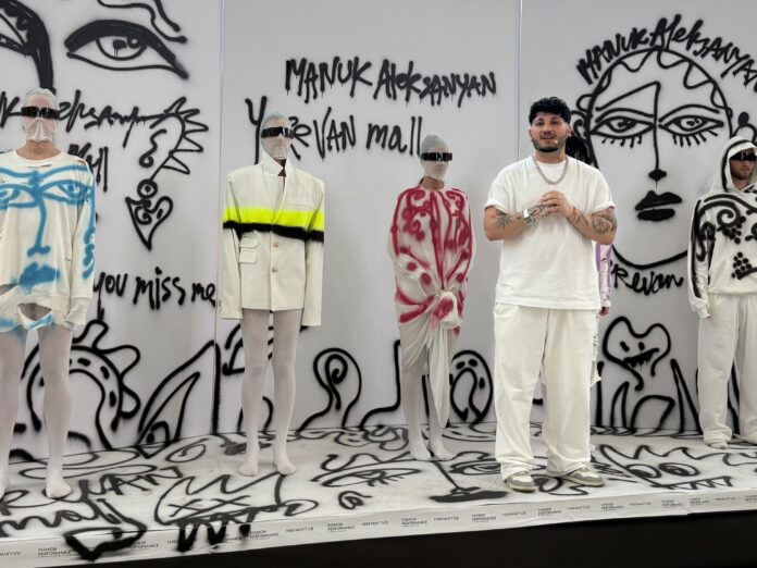 Manuk Aleksanyan standing beside models wearing hand-painted garments during a live fashion performance at Yerevan Mall.